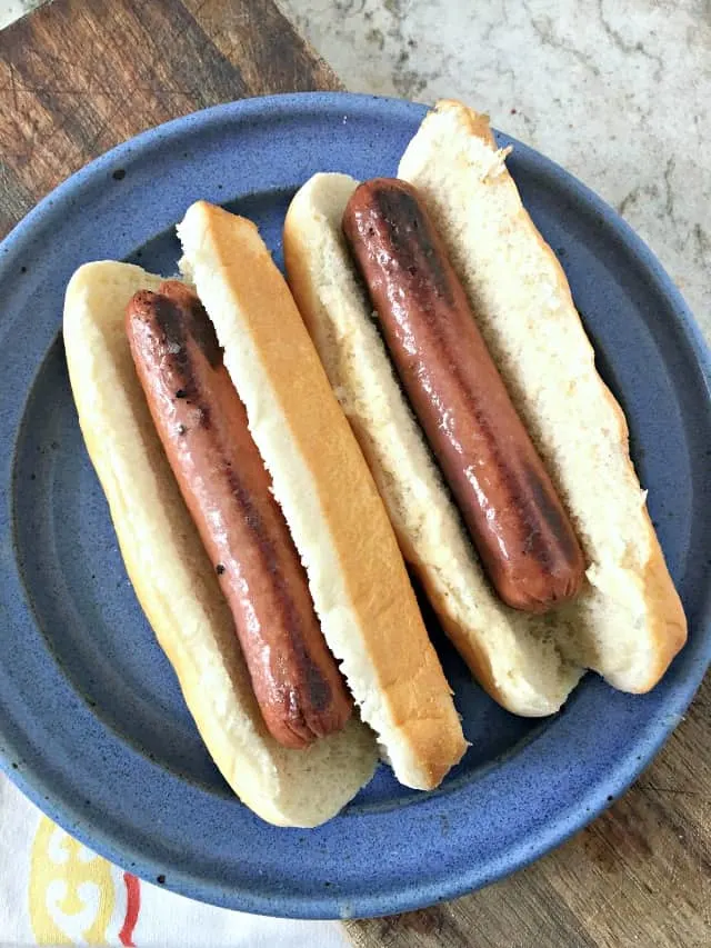 Two Hot dogs resting in buns on a blue plate on a cutting board.