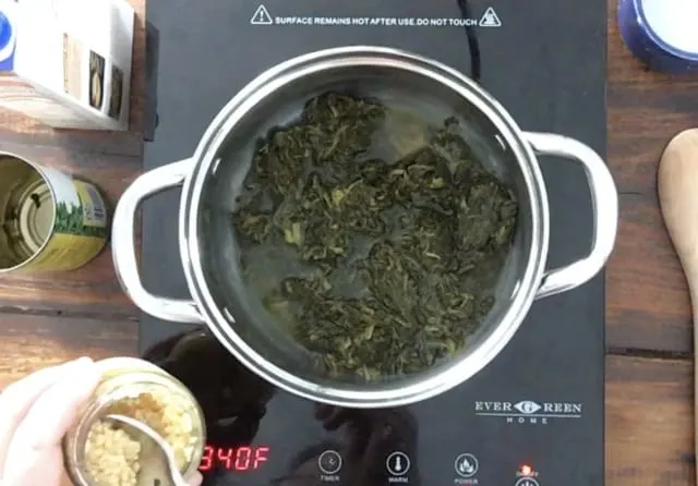 Minced Garlic being added to the spinach in the saucepan