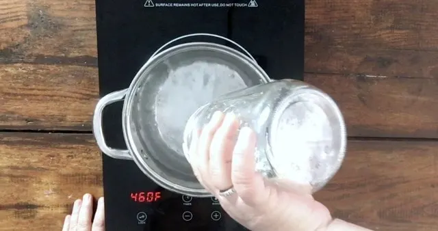 a hand pouring a quart jar of water into a sauce pan