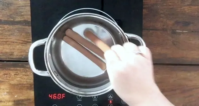 Hand adding three hot dogs to a sauce pan