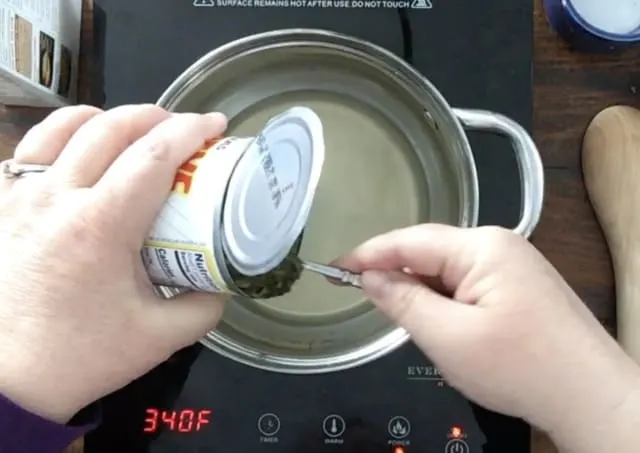 a hand scooping canned spinach into the saucepan for how to cook canned spinach