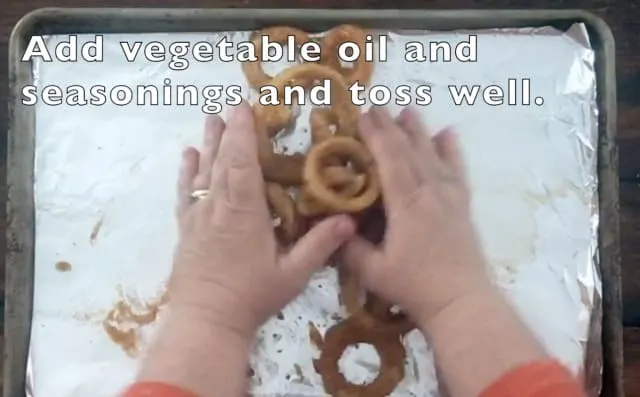 two hands tossing onion rings, oil and seasonings on a baking sheet