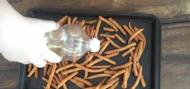 hand pouring oil on frozen sweet potato fries on pan