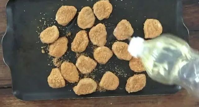 Pouring vegetable oil onto the frozen chicken nuggets