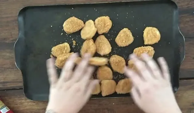 two hands spreading chicken nuggets onto a baking sheet