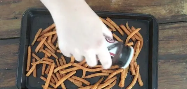hand sprinkling season salt onto sweet potato fries