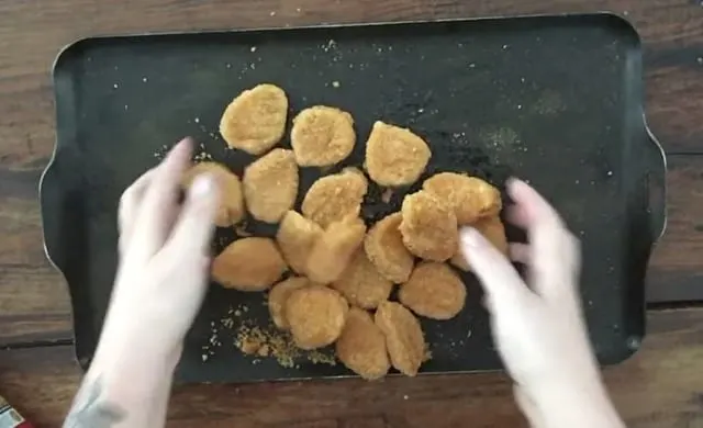 Two hands mixing oil and spices onto the frozen chicken nuggets