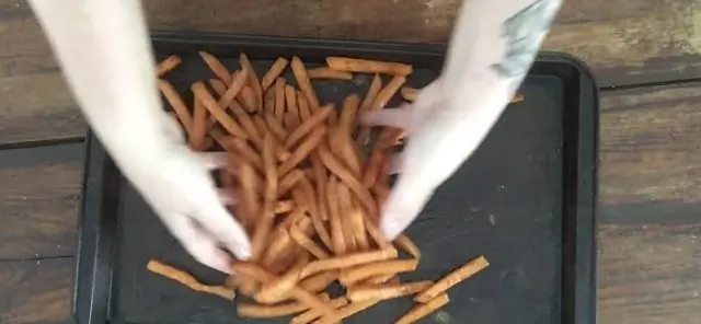 two hands mixing up sweet potato fries, seasoning and oil on pan