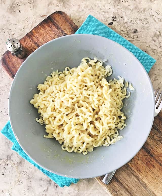 gray bowl of ramen with blue napkin and cutting board