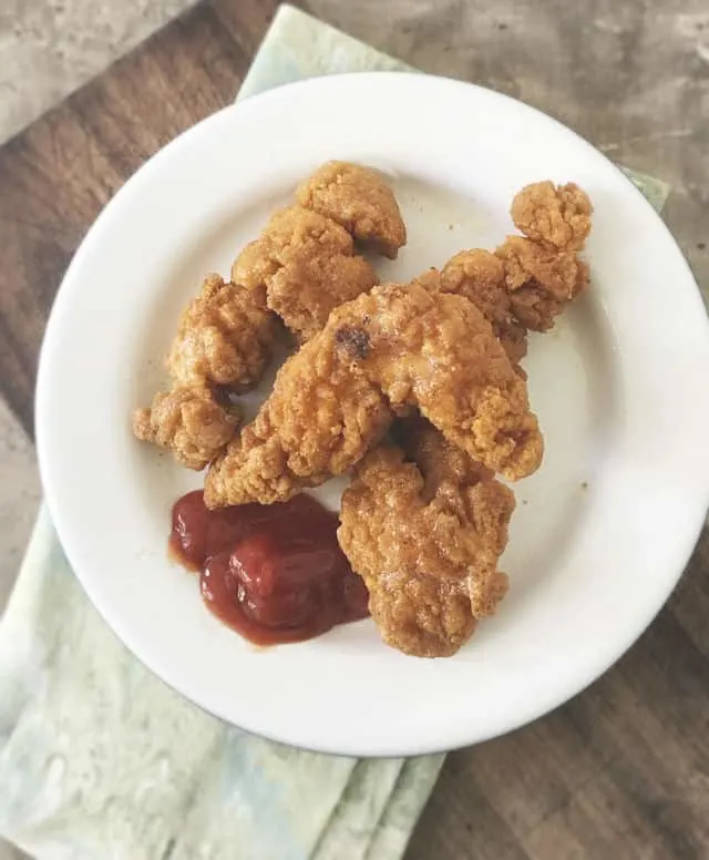 Overhead photo of three chicken strips on a white plate