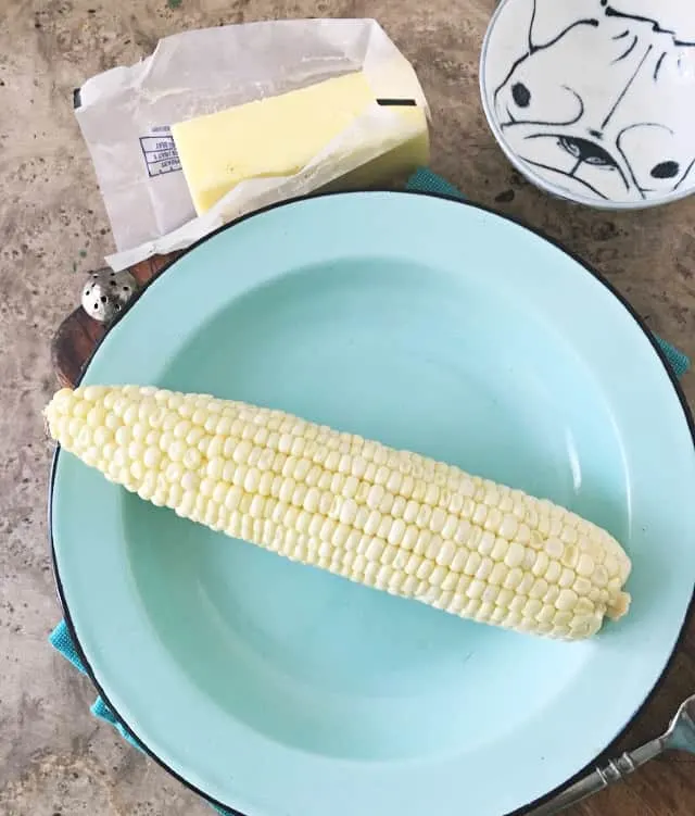 ear of corn on a blue plate butter in background