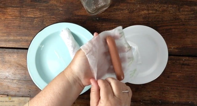 hand wrapping hot dog with damp paper towel blue plate background