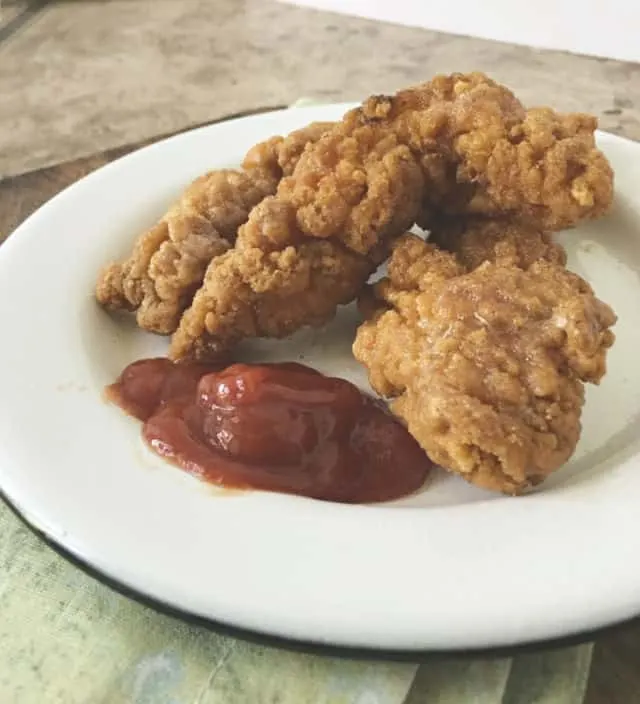 Side view of chicken tenders on a plate with ketchup