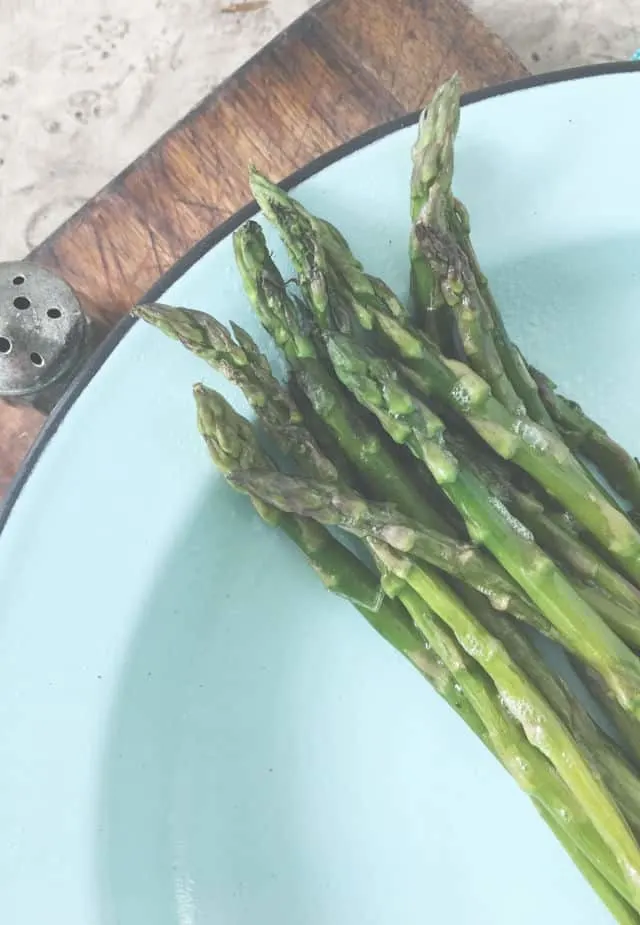 Green asparagus tips on a blue plate with salt shaker