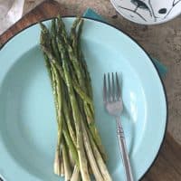 whole asparagus on blue plate with fork and butter in back ground