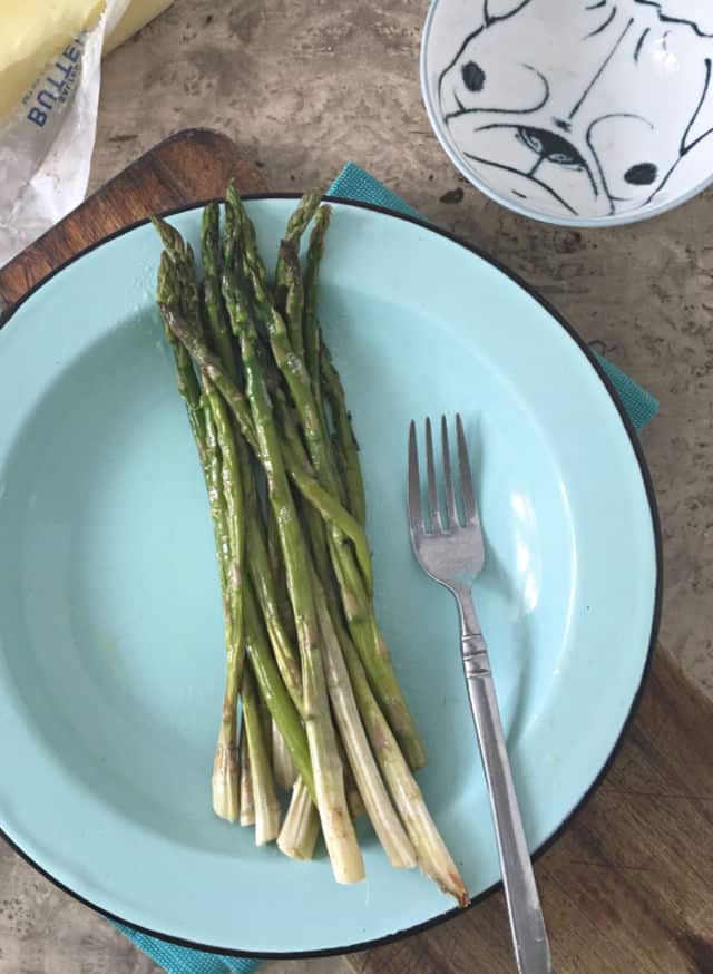 whole asparagus on blue plate with fork and butter in back ground