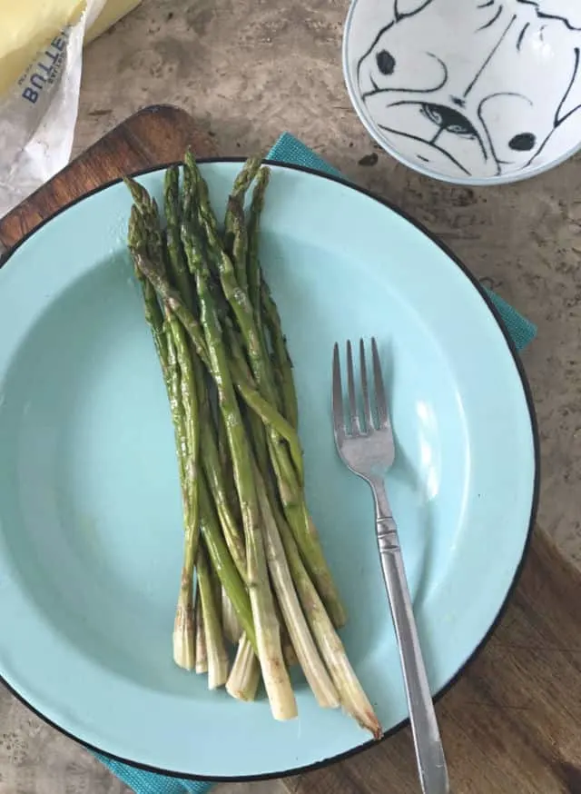 whole asparagus on blue plate with fork and butter in back ground