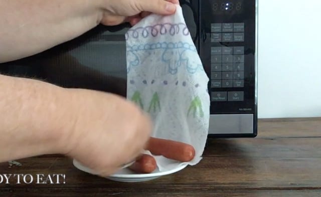 Hand unwrapping hot dog from wet paper towel