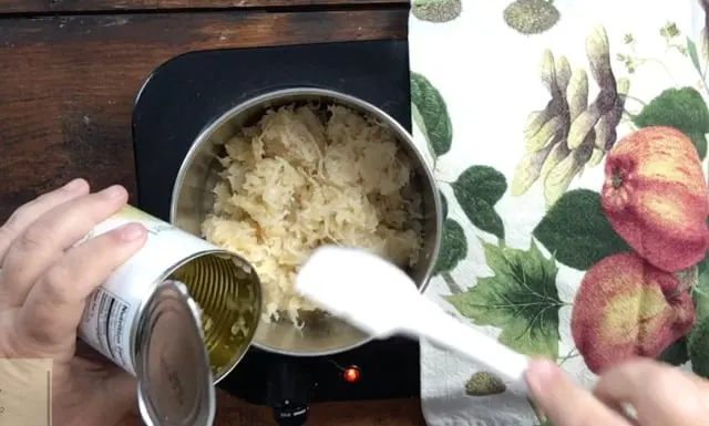 hand with spatula adding canned sauerkraut to saucepan