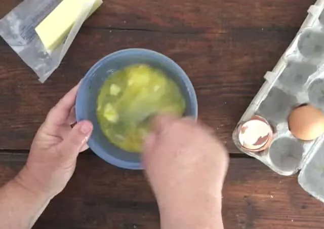 two hands mixing the eggs and other ingredients in bowl