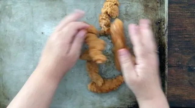 Hands mixing frozen chicken strips with oil and seasonings