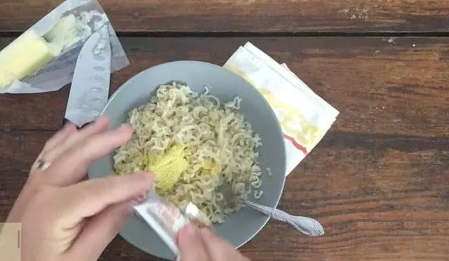 Hands adding flavoring and butter to ramen noodles