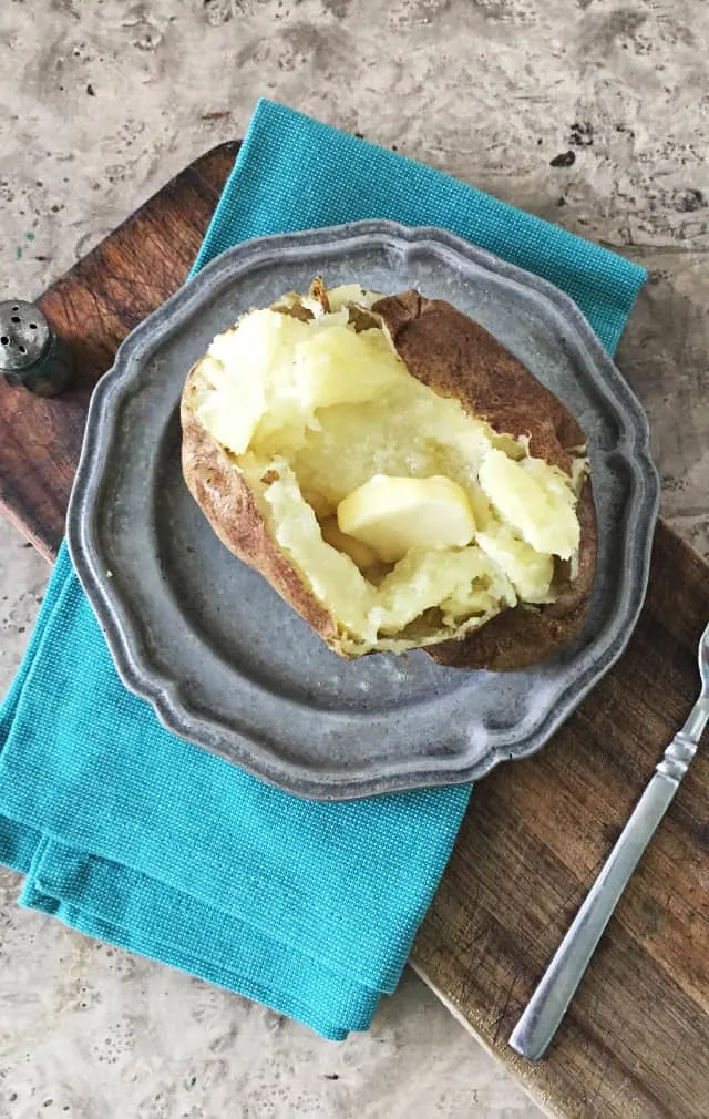 overhead shot of butter melting on top of baked potato with blue napkin and fork