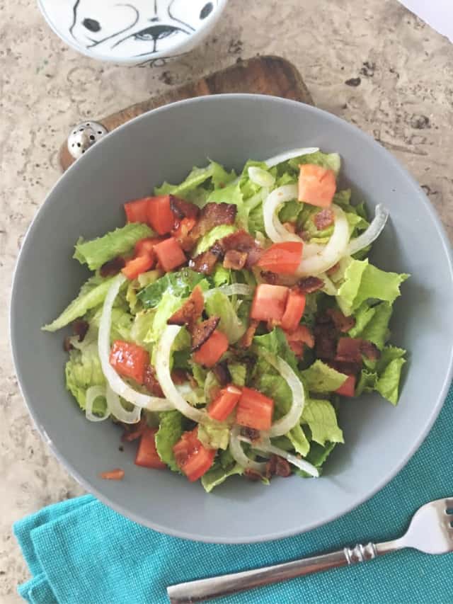 overhead shot of southern wilted lettuce salad in gray bowl with blue napkin