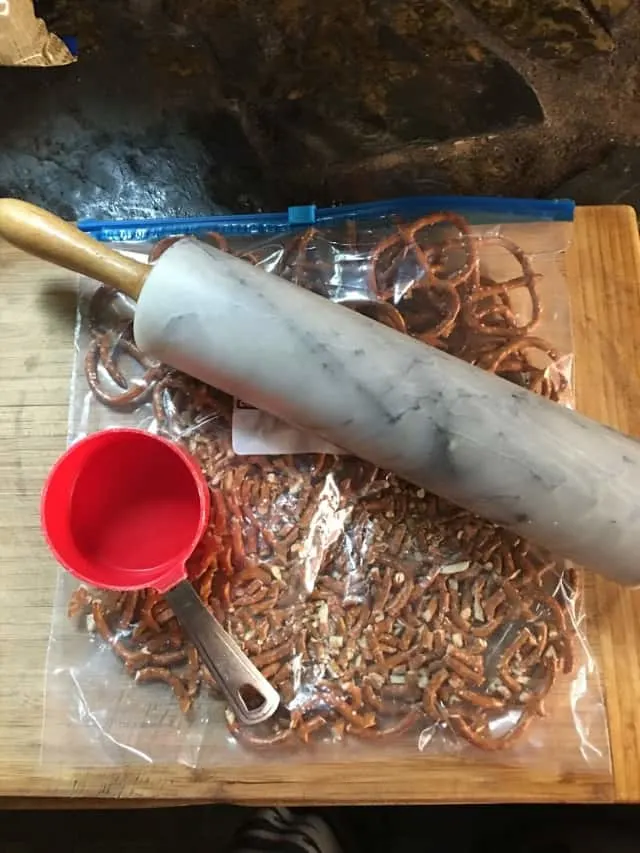 Crushed pretzels with measuring cup, rolling pin and cutting board