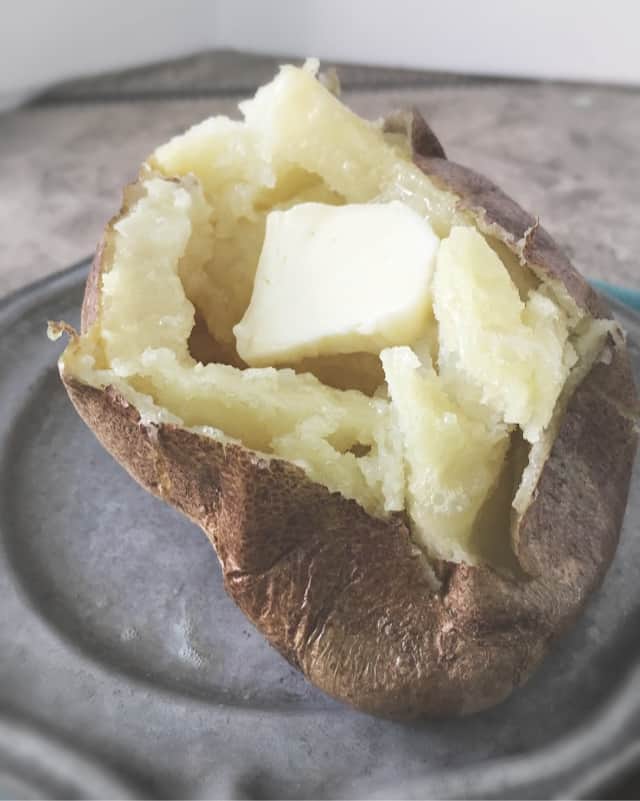 side view close up of baked potato with pat of butter on gray plate