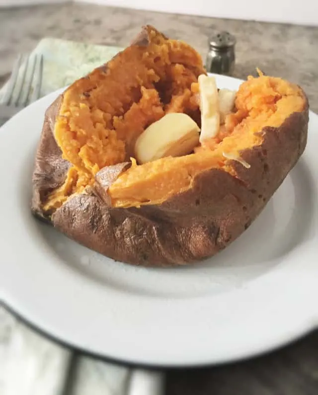 side view of a sweet potato with a pat of butter on a white plate