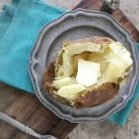 overhead photo of baked potato with butter on gray plate on blue napkin