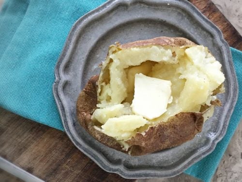 overhead photo of baked potato with butter on gray plate on blue napkin