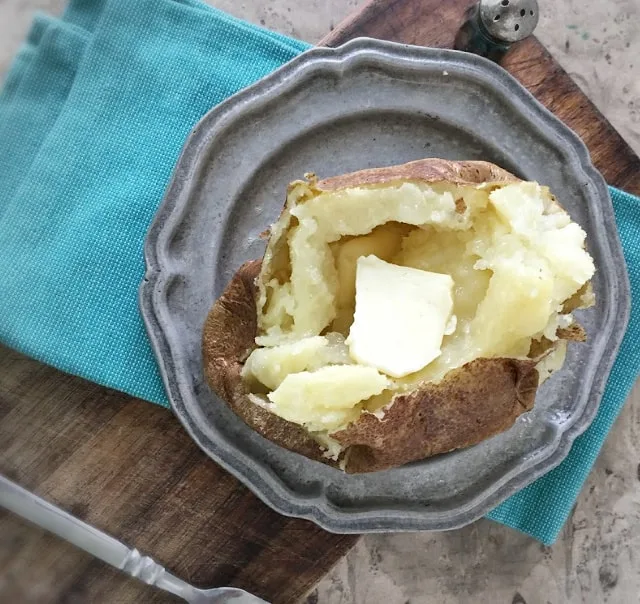 overhead photo of baked potato with butter on gray plate on blue napkin