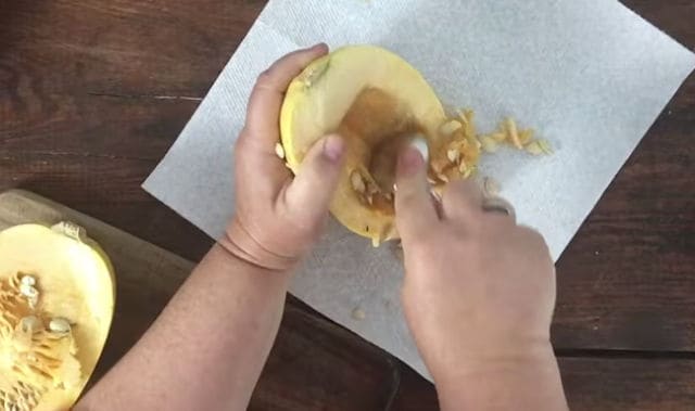 two hands removing the seeds from the middle of a squash