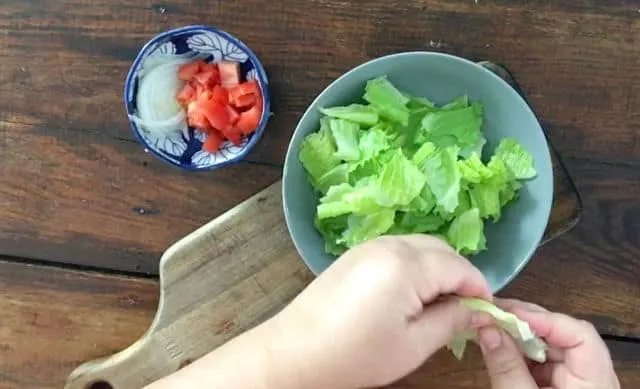hand tearing up lettuce into a bowl on wooden table