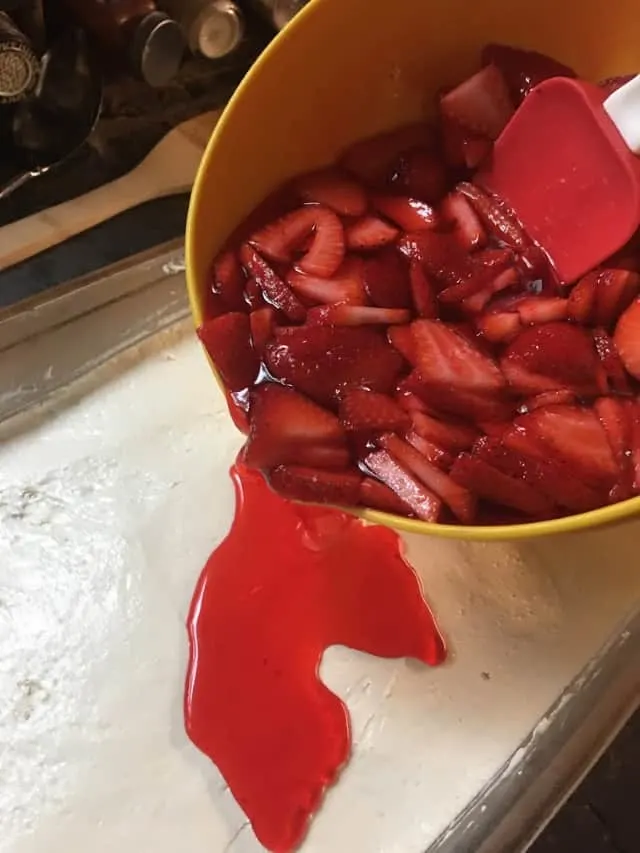 bowl pouring the jello mixture on top of the cool whip mixture in baking dish