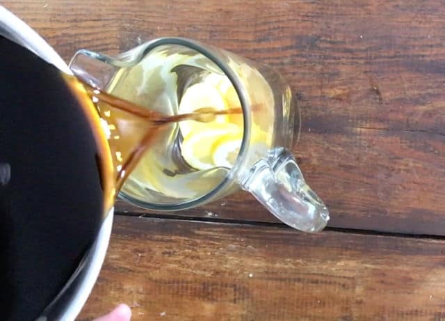 pitcher pouring tea into a glass pitcher with lemon slices in it