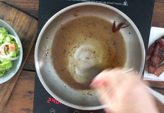 hand whisking bacon grease with other dressing ingredients in frying pan