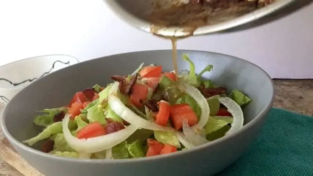 pouring the bacon vinegrette over the wilted lettuce salad