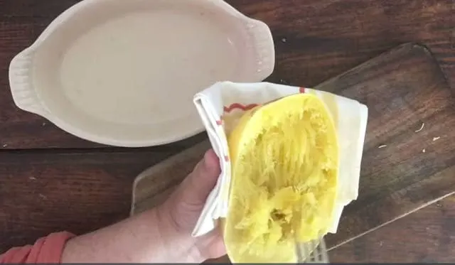 hand holding the squash and hand using fork to scrape the spaghetti squash to remove the spaghetti