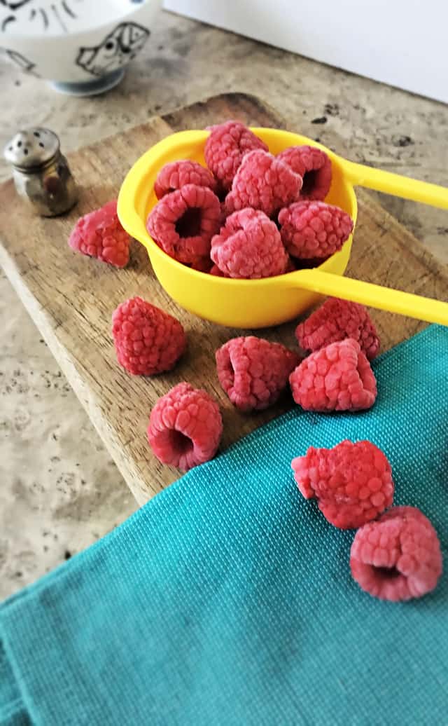 yellow half cup measure with raspberries on blue towel