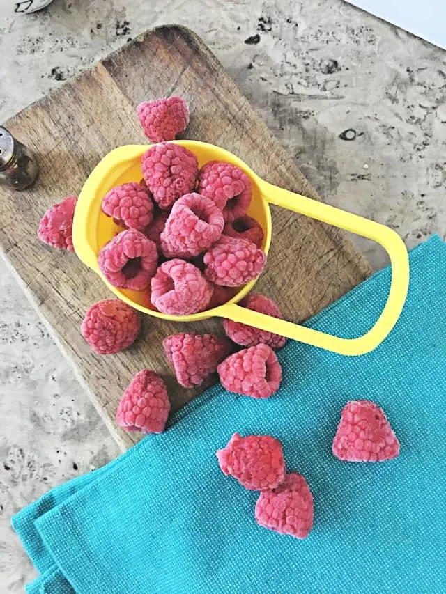 cup holding frozen raspberries on wooden background