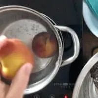 hand dropping peach into boiling water