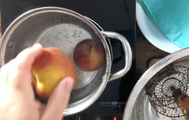 hand dropping peach into boiling water