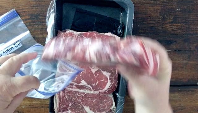 hand placing a ribeye steak into a zip lock freezer bag