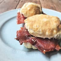 Two country ham biscuits on a blue plate on wooden table