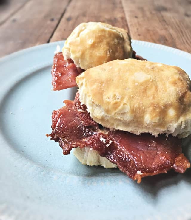 Two country ham biscuits on a blue plate on wooden table