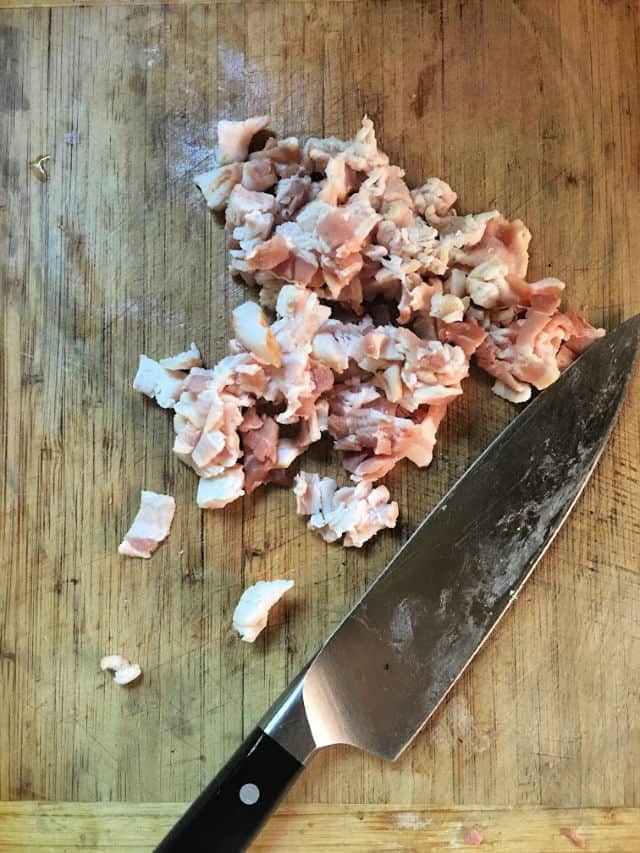 raw bacon chopped on cutting board with chef knife