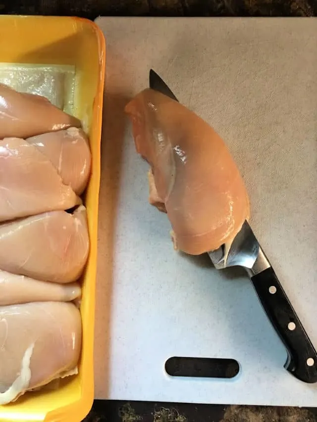 chicken breast being cut in half with chefs knife